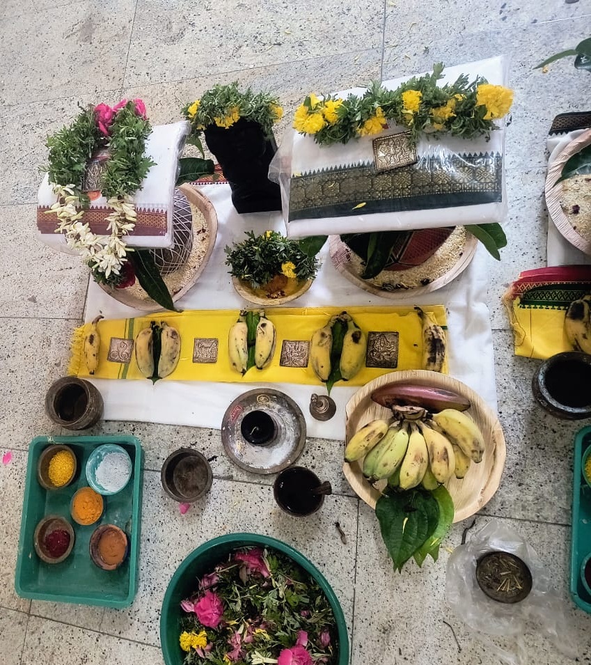 Close-up of arranged pooja items including flowers, diya lamps and ritual accessories